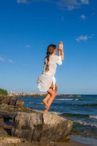 A woman in a yoga pose on a rock by the ocean, enjoying a sunny day.